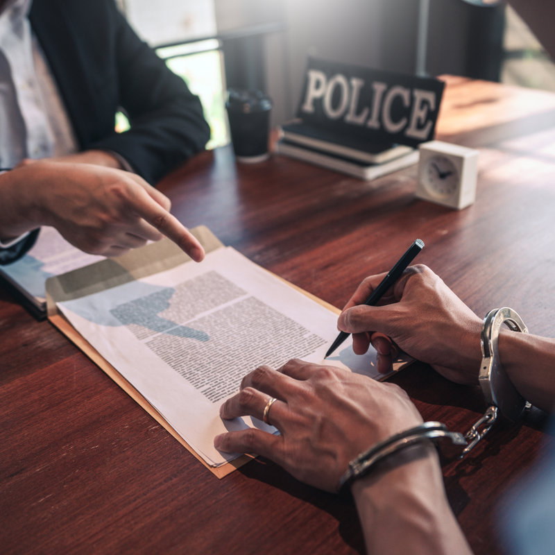 individual in handcuffs signing documents next to a police officer