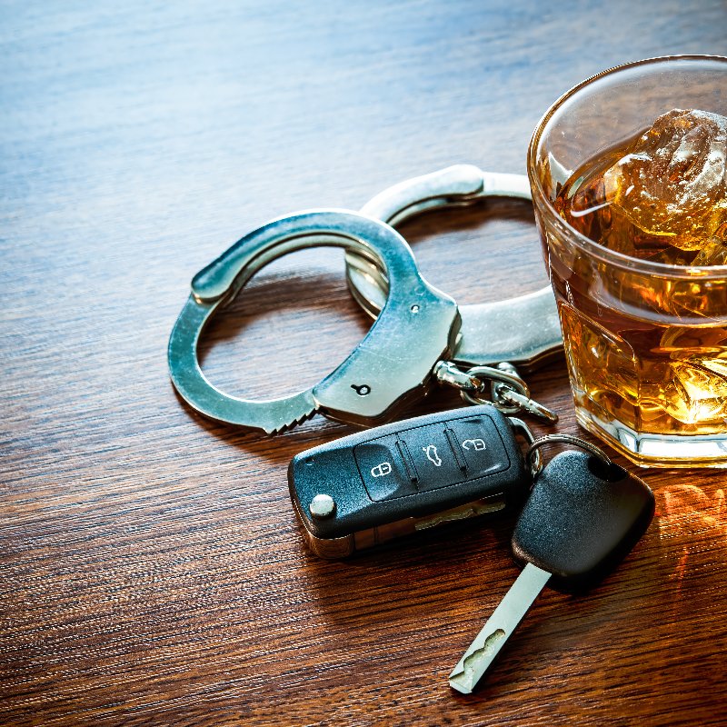 car keys, a glass of alcohol, and handcuffs sitting together on a table