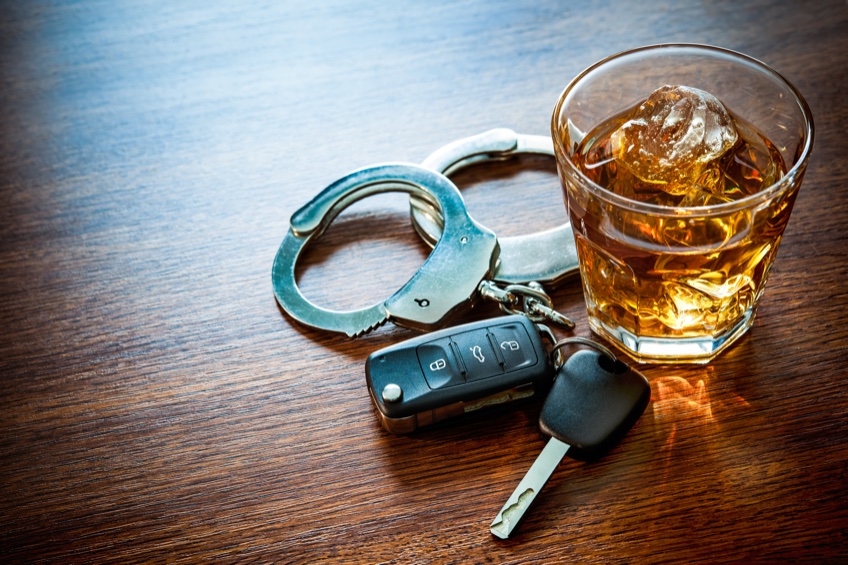 handcuffs, keys with alcohol drinks in background signifying DUI