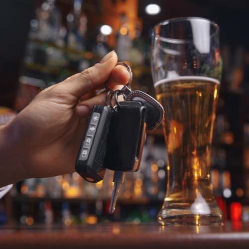 hands and keys with alcohol drinks in background signifying drunk driving