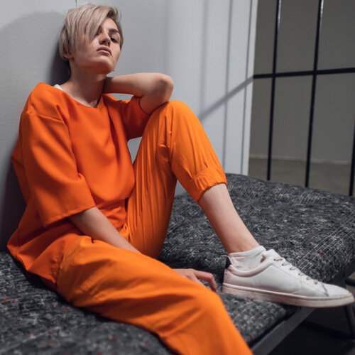 Woman wearing an orange jumpsuit sitting in a prison cell.